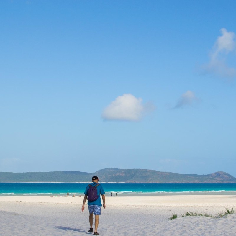 a man walking across a beach next to a body of water